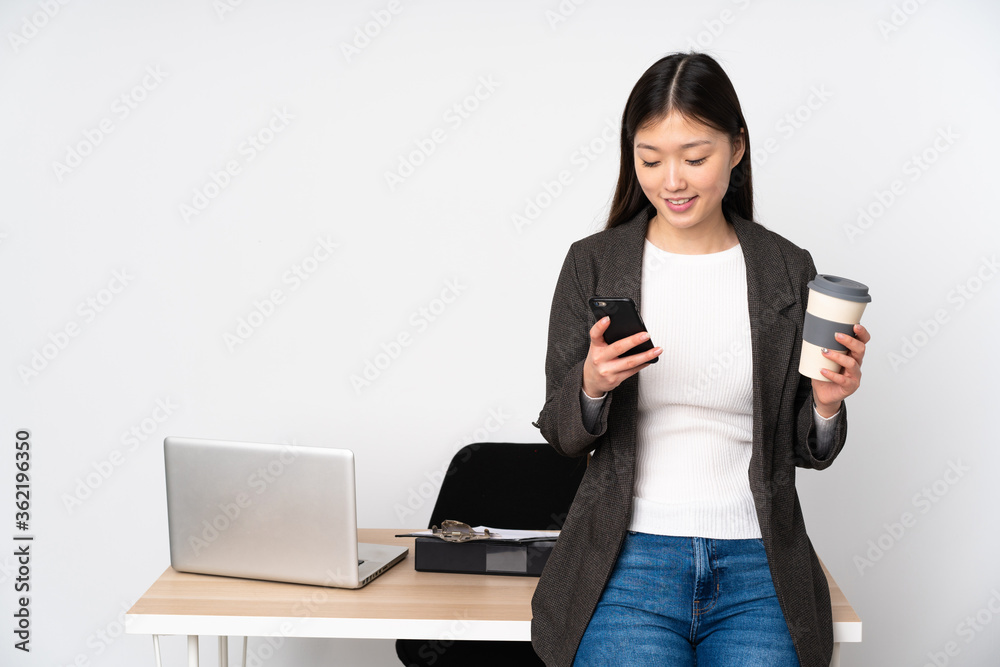 Business asian woman in her workplace isolated on white background holding coffee to take away and a mobile Business asian woman in her workplace isolated on white background holding coffee to take away and a mobile