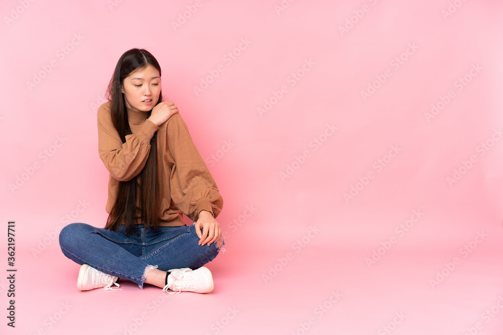 Young asian woman sitting on the floor isolated on pink background suffering from pain in shoulder for having made an effort Young asian woman sitting on the floor isolated on pink background suffering from pain in shoulder for having made an effort