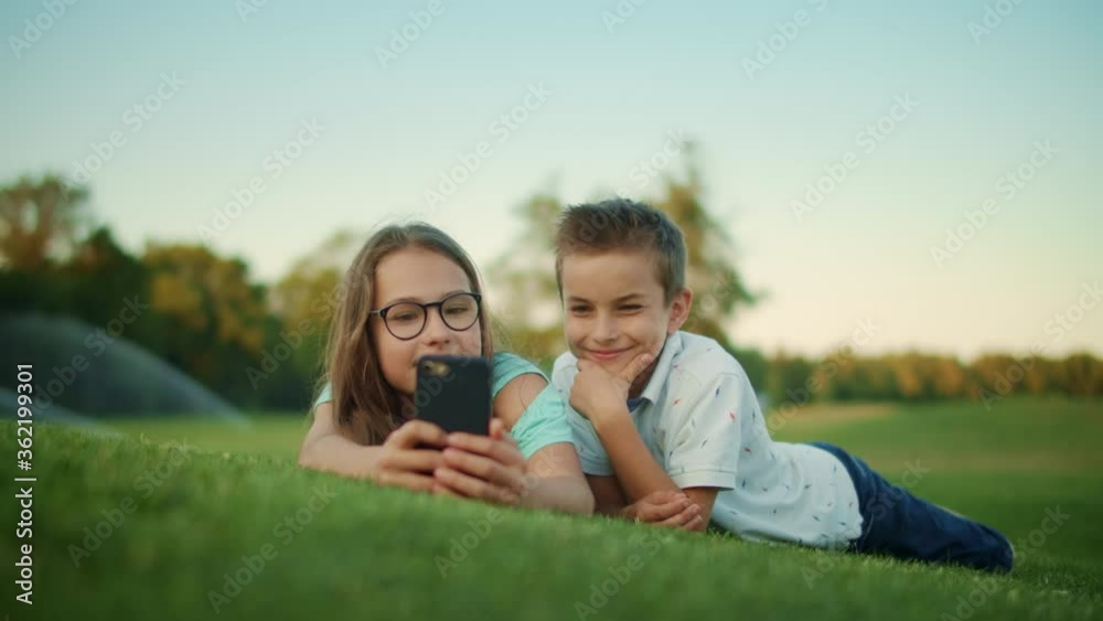 Siblings lying on grass in field. Laughing girl and boy using smartphone outdoor Siblings lying on grass in field. Laughing girl and boy using smartphone outdoor