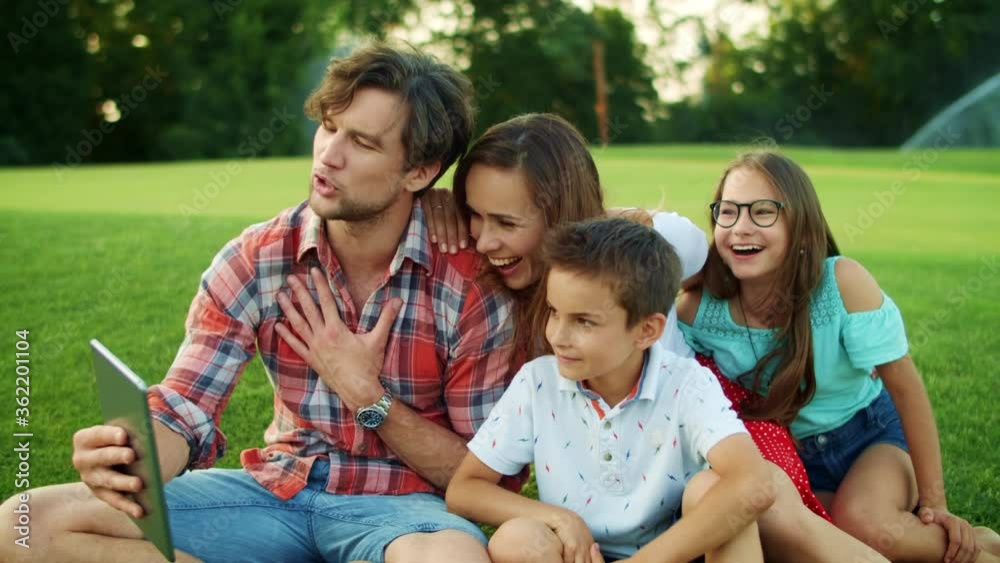 Parents and children using tablet in park. Family having video call on pad Parents and children using tablet in park. Family having video call on pad