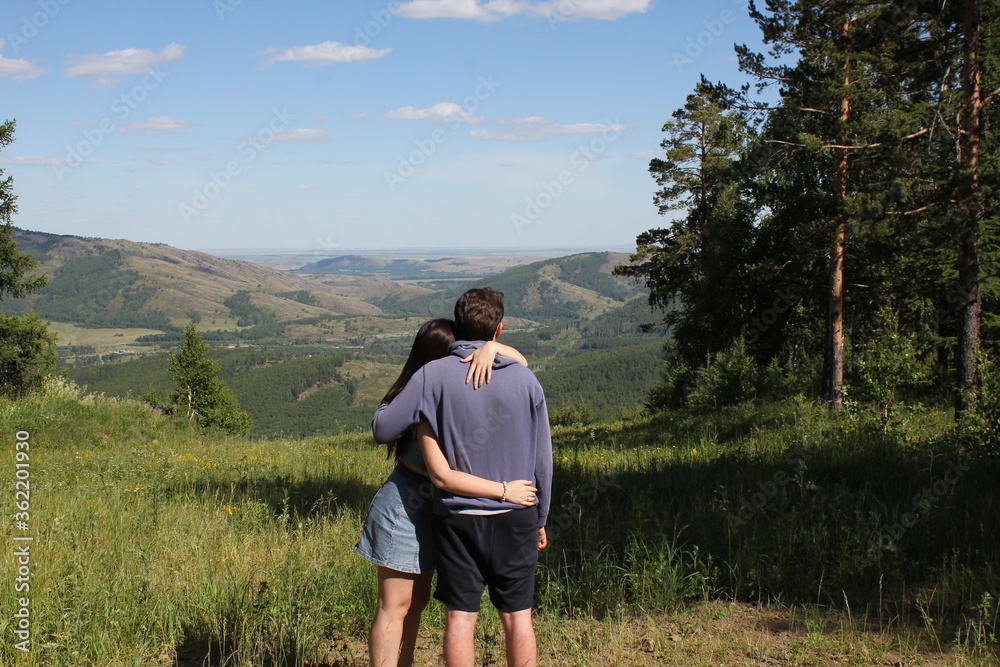 A guy and a girl standing on top of a mountain, admiring the panoramic top view of the mountains, hills, sky