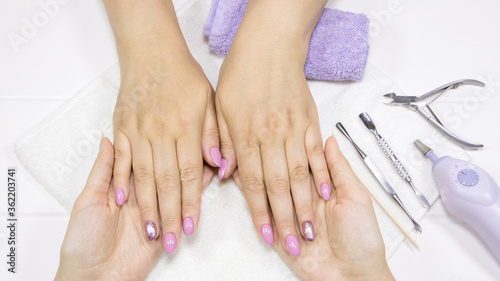  A woman shows her hands with painted nails. The manicurist holds the client's hands. Pink, Nude manicure, nail art, glitter Polish. Spa hand care. Beauty salon, hand massage. Feminine, makeup.
