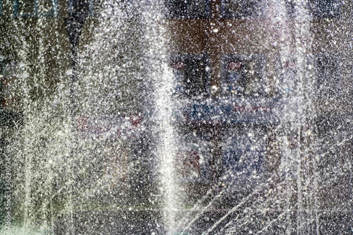 Shot of young boy having fun cycling through a fountain on a hot summer day in a park. Drops of water froze in the air. The concept of a happy childhood.