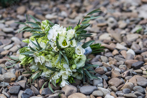  Bridal bouquet of white eustomas and greenery on sea stones from a side angle in natural light.