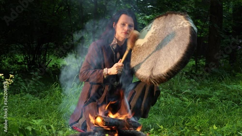 Shamanic woman conducts ritual at night in the forest by the fire. Ethnic traditions
