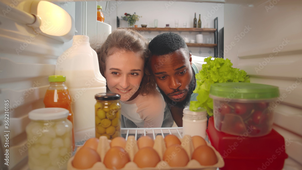 Diverse young couple taking food for snack from fridge