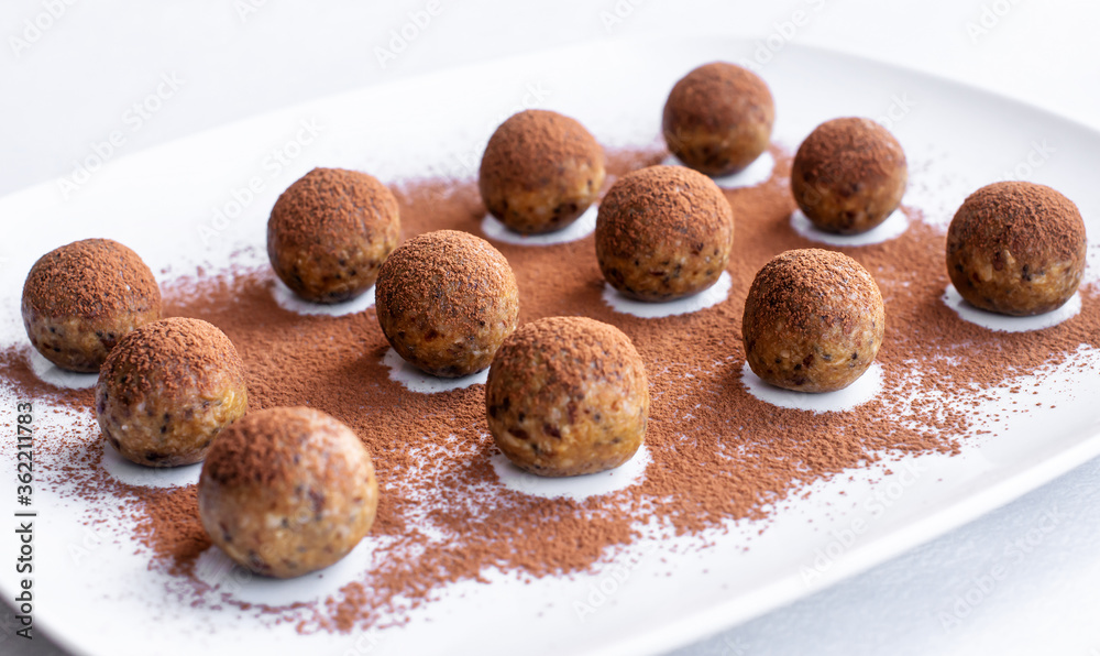 Useful, delicious energy balls lie on a white dish, sprinkled with cocoa. A nutritious home-made product made from oat flakes, nuts and seeds. Close-up, selective focus. Useful, delicious energy balls lie on a white dish, sprinkled with cocoa. A nutritious home-made product made from oat flakes, nuts and seeds. Close-up, selective focus.