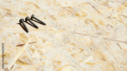 Three black metal tapping screws lie on a wooden surface, free space for text, top view