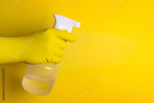 Homem com luva de proteção amarela segurando um spray de alcool líquido 70 sobre o fundo amarelo
 photo