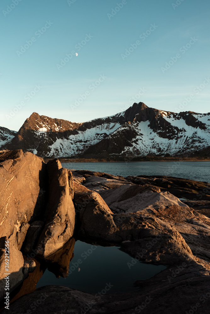 Moon reflection in the calm water, snowy mountains and sea in the background. Beautiful sunset light during summer time. Polar day on Senja island, Norway. 