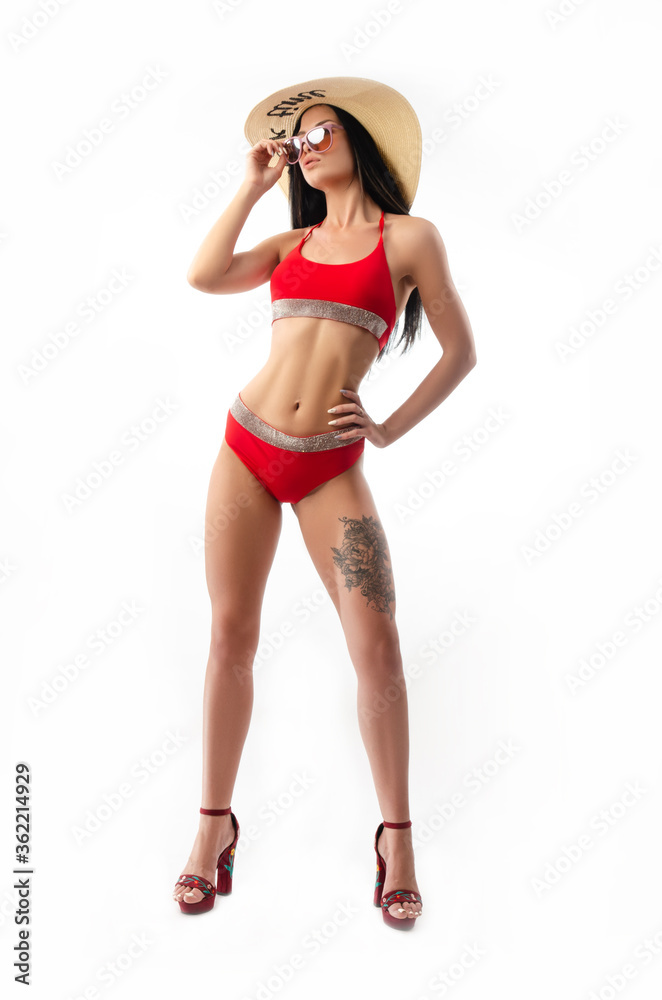 Naklejka premium brunette in a red swimsuit, slim and sexy in a summer hat isolated on a white background