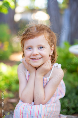 Little girl with red hair smiling sweetly on a summer day. 
