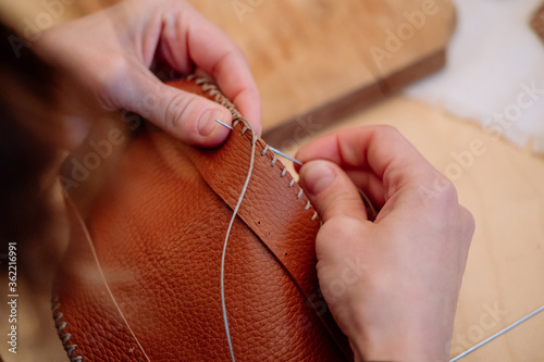 Detail shot of woman's hands sewing a brown piece of leather with a needle
