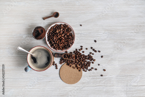 Photo of fresh tasty coffee on light wooden background. Coffee cup  coffee beans  ground powder and beer coaster. Top view. Flat lay.