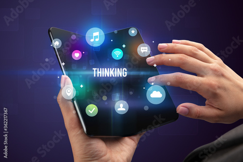 Businessman holding a foldable smartphone with THINKING inscription, social media concept