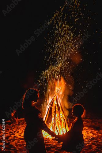Silhouette of two girls on the background of a big bonfire in a summer scout camp.