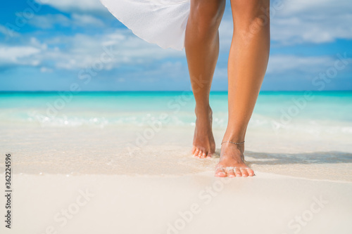 Elegant woman on luxury Caribbean beach vacation relaxing in summer tropical ocean background. Relax feet and legs walking enjoying sun tan lifestyle.