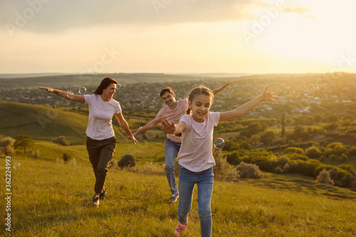 Family having fun with smiles runs along the grass on nature in the evening at sunset.
