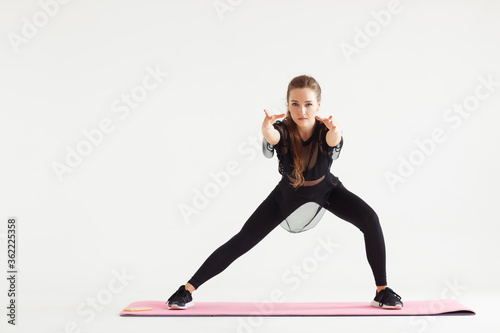 Young attractive yogi woman practicing yoga, doing Utthita Trikonasana exercise, extended triangle pose, working out, wearing sportswear, black pants and top, indoor full length, white yoga studio