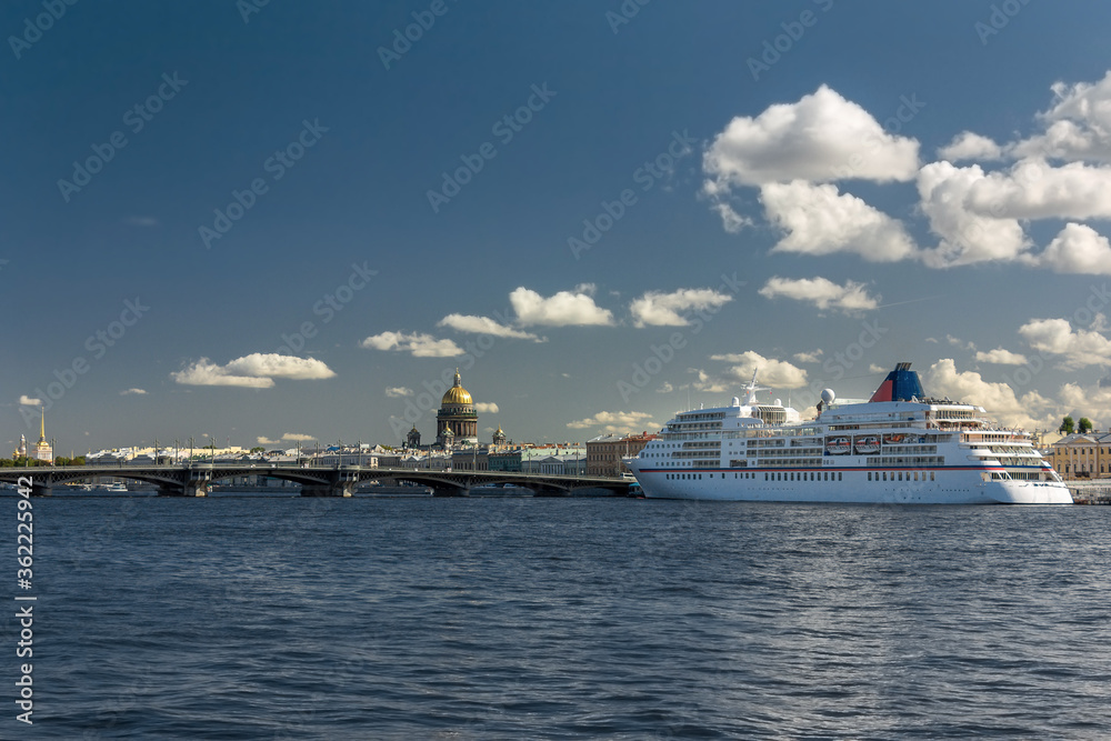Large cruise ship on the pier near the embankment of the old city. Low point photo of a bay with splashing waves on a bright day