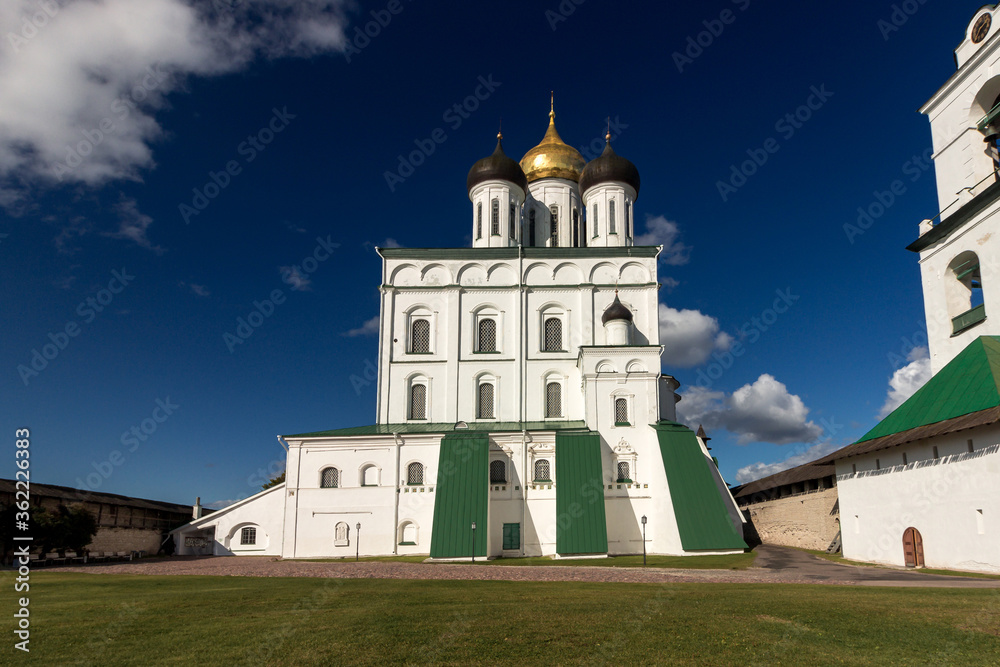 View of the Pskov Kremlin near the city river on a summer clear day. Trails for walking tourists. View of the Pskov Kremlin near the city river on a summer clear day. Trails for walking tourists.