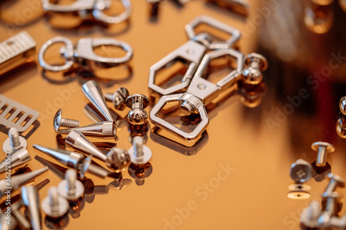 Silver handbag accessories, rivets, screws, carabiners placed on a gold reflective plate