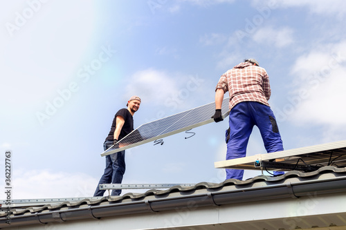 Electrical engineers mans are working installing solar panel on solar station on roof against blue sky. Development sun alternative energy technology. Ecological concept.
