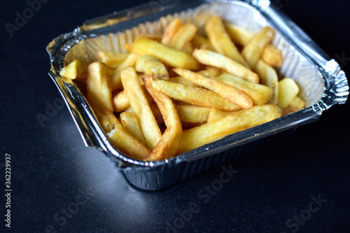 Delicious French fries in an aluminum container on a black background
