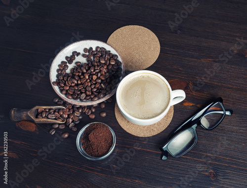 Fresh delicious coffee. Coffee cup, coffee beans, ground powder, beer coaster and glasses on wooden background.