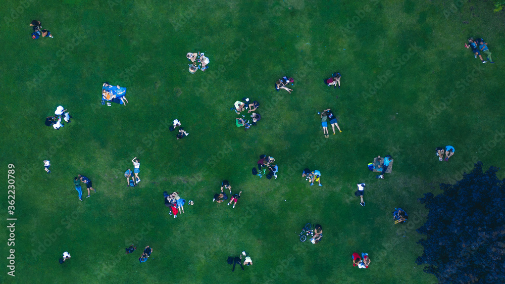 Obraz premium Top View Many people rest on a green lawn. Social distance while relaxing on the lawn after quarantine. Drone Photo 90 degrees. Groups of friends spend a weekend outdoors.