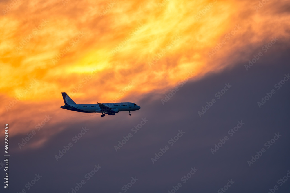 Fototapeta premium Airplane landing on orange cloudy dramatic sunset. Travel concept.