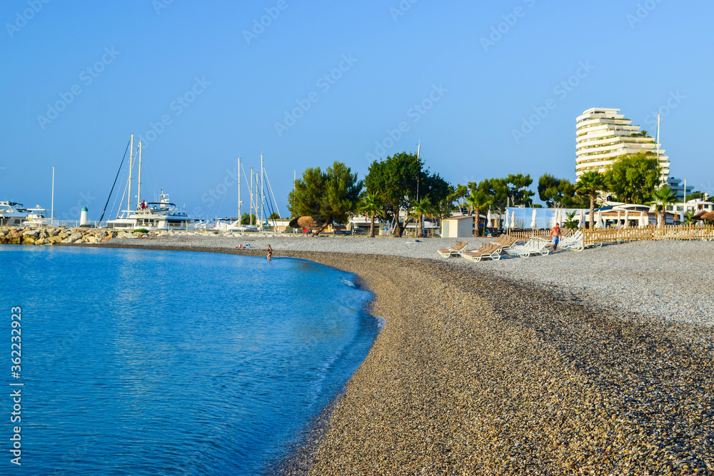 Landscape of the beautiful pebble beach of the Cote d'Azur at sunny morning. Beach holidays by the calm Mediterranean Sea. France.