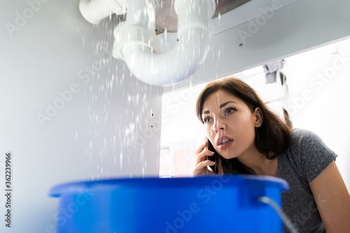 Women Doing Emergency Plumber Phone Call In Kitchen