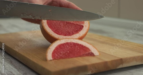 Female hands cut a half of juicy grapefruit with knife into round pieces.