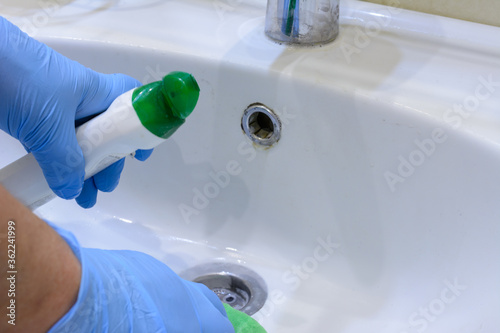 Cleaning the bathroom. Woman is cleaning sink and faucet with spray detergent. Close-up. © Evgeniy