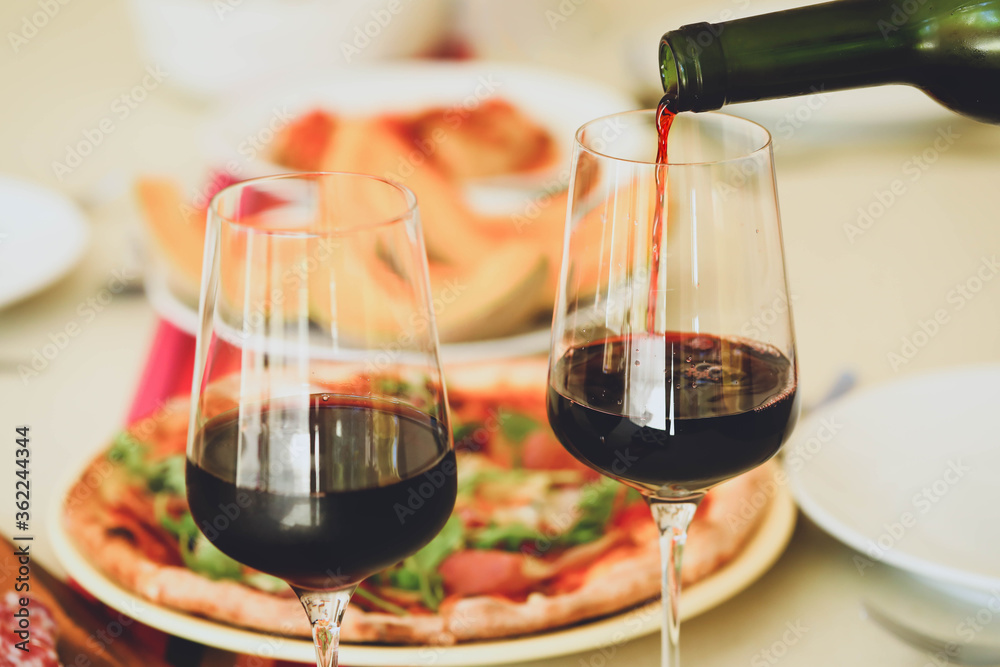 Pouring red wine from bottle into  glasses on table with food background