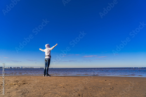 Silhouette of a woman on the beach from afar. A woman in jeans looks out at the sea at dawn. Space for text.