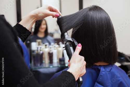 The hairdresser does aligns the hair with hair iron to a young girl, brunette in a beauty salon. Professional Hair Care and treatment for brittle hair.