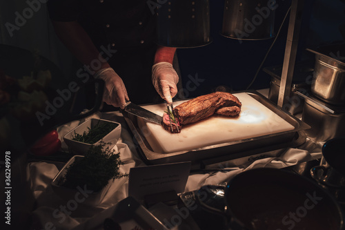 Man slicing piece of grilled beef filet meat on white kitchen board and serving it with rosemary. Celebration, party, birthday or wedding concept.