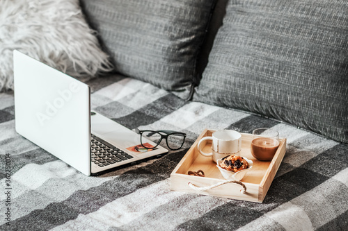 An open laptop and a wooden tray with dessert on the sofa. Working home environment. Offline work.