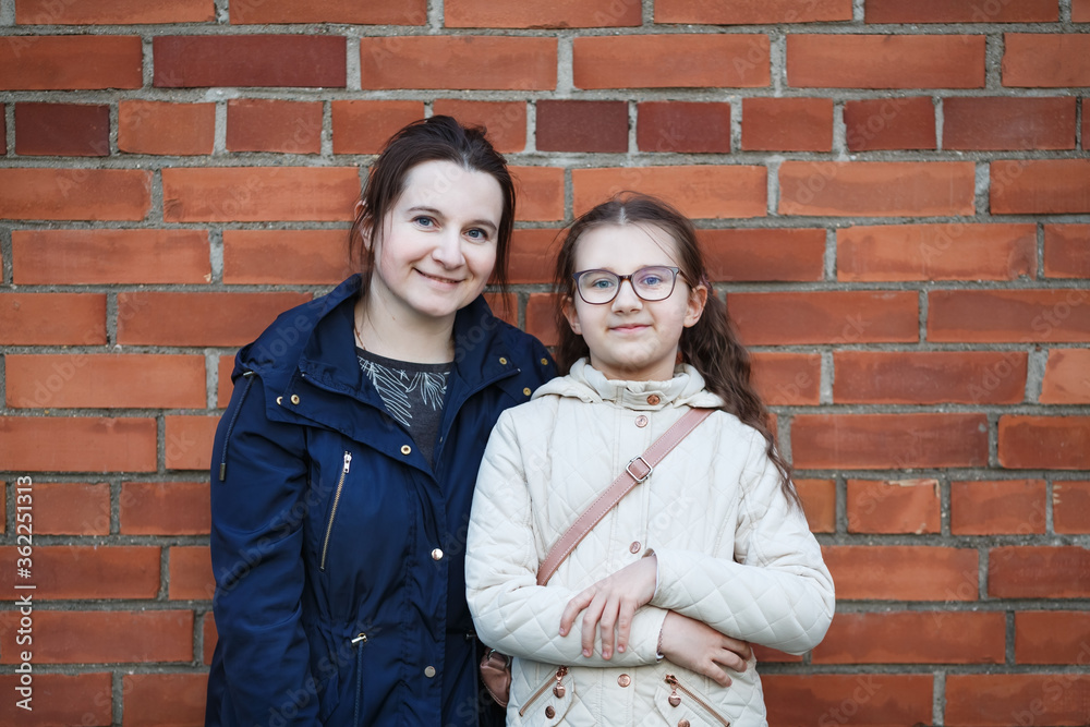 Mom and daughter against brick wall background. Woman and girl.