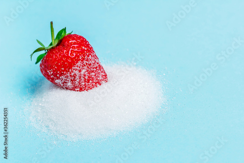 One berry of ripe delicious strawberries lie on sugar on a blue background. Background with strawberries. Summer berries. Free space in the photo.