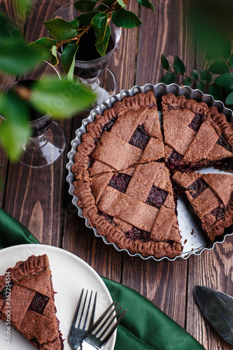 Hommade chocolate berry fruit pie on wooden background with green leaves, summer pie outdoors, piece of pie on the plate