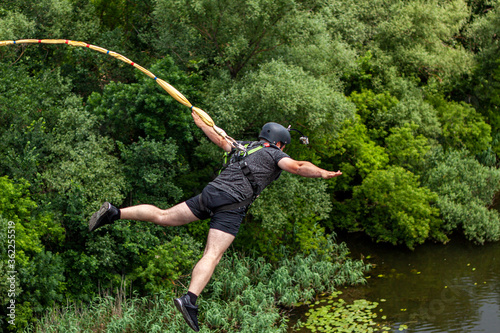 Ivanovsky Bridge, Ukraine - June 21, 2020: Concept of Extreme Sports and Fun. The man is doing rope jumping from the bridge. He is very happy to make a dream come true.