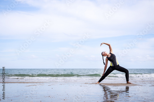 young Asian woman is stretching or warm-up her body in yoga pose before exercise by running on the beach female fitness model portrait. Concepts of exercise and good health.