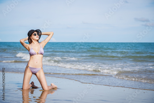 Outdoor summer portrait of Asian beautiful girl in a sexy bikini sitting on the beach in summer. teenage girls. sexy body. concept vacation, holiday in summer and blue sky