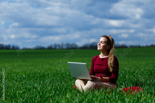 Joyful young girl on the grass with a laptop on her lap. He raised his hands up and laughed. Happiness in the lifestyle of a classical student. Work on the nature. Rest after a good working day.