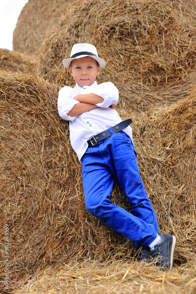 A cute boy is high under the sky on a haystack in the hay season. A cute boy is high under the sky on a haystack in the hay season.