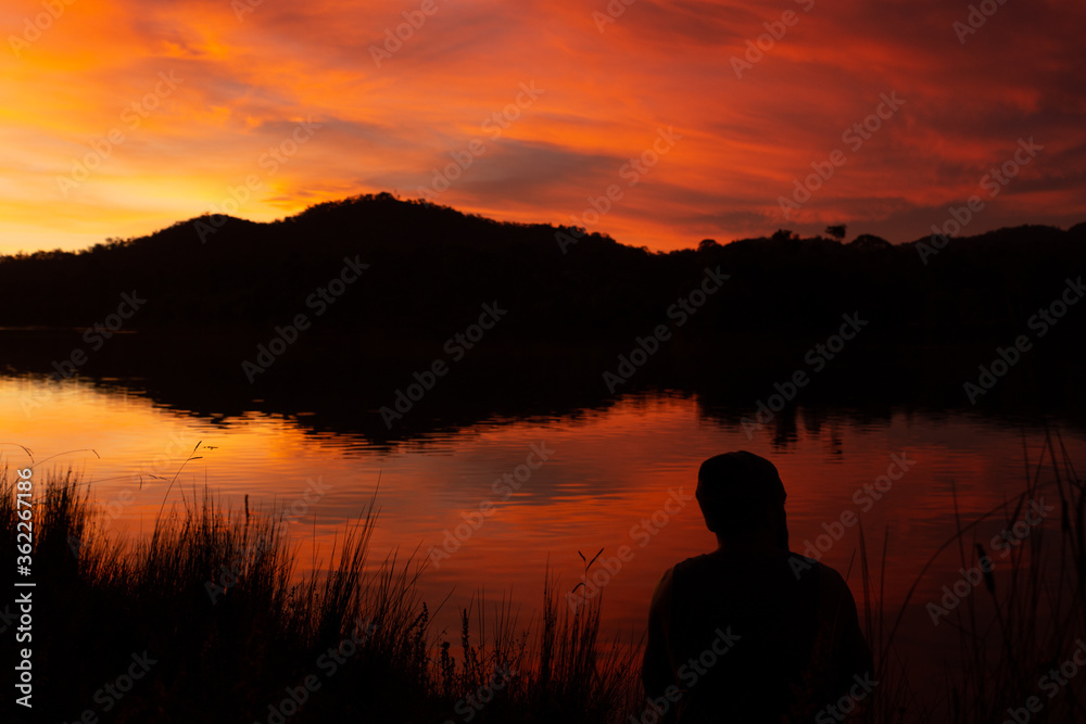 Orange skies reflecting on lake showing a man in silhouette