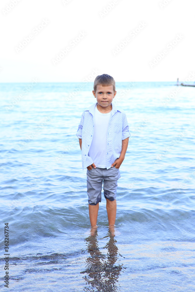 Beautiful boy stands on the seashore in summer